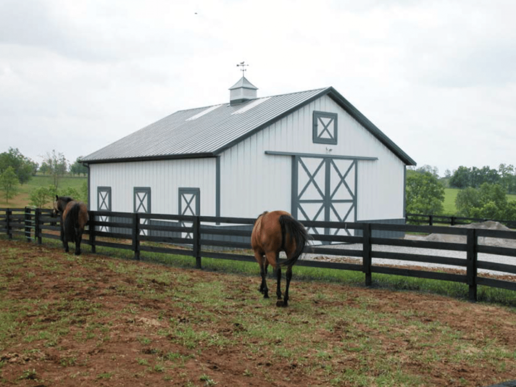 Crossbuck Sliding Doors Post-frame horse barn with crossbuck sliding doors and black fence in front.
