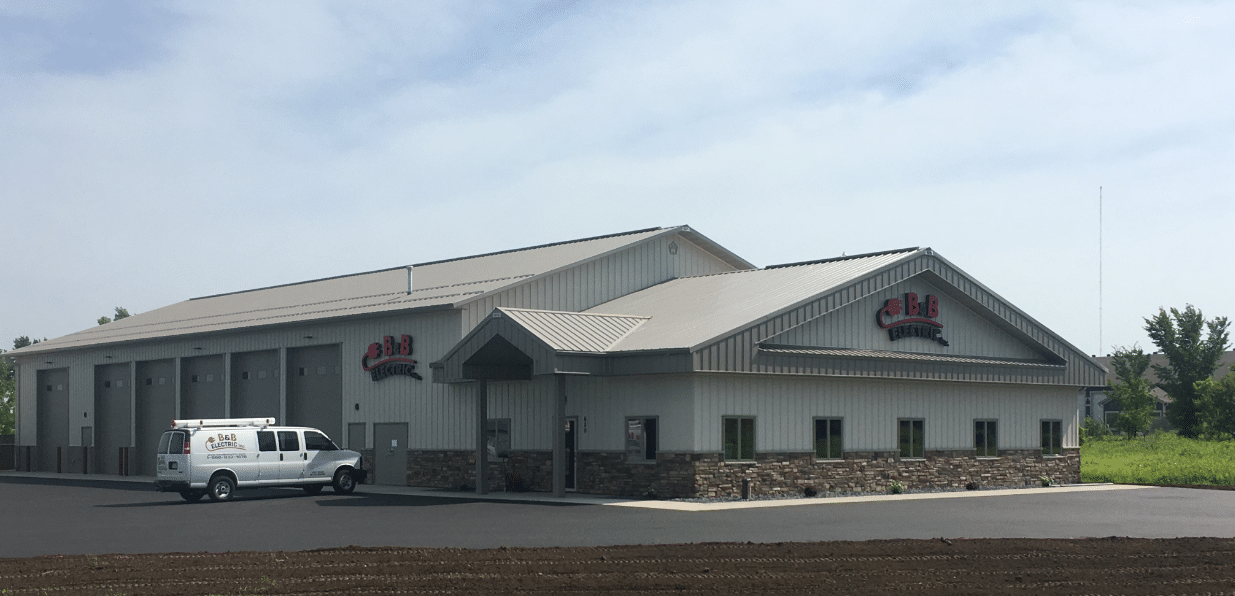 Steel-clad post-frame building for an electrical contractor with multiple overhead doors and stone wainscot.