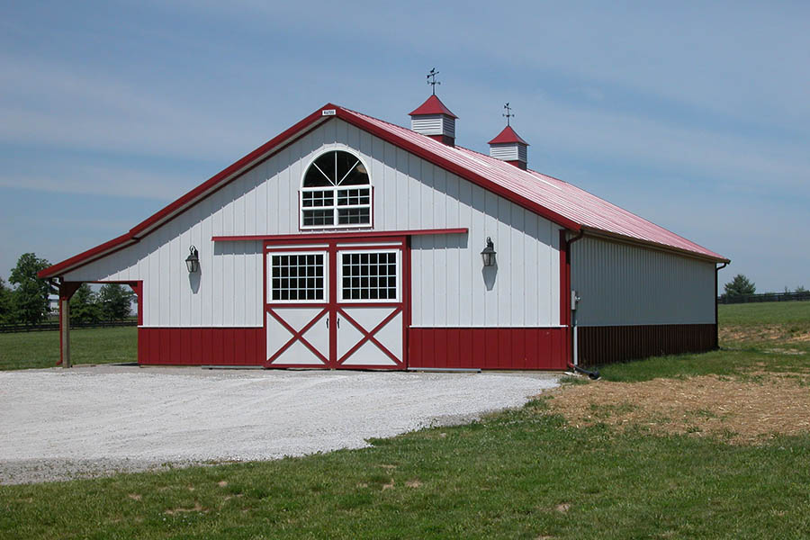 Post-frame pole barn with sliding doors, cupolas, wainscot, and classic barn-style features.