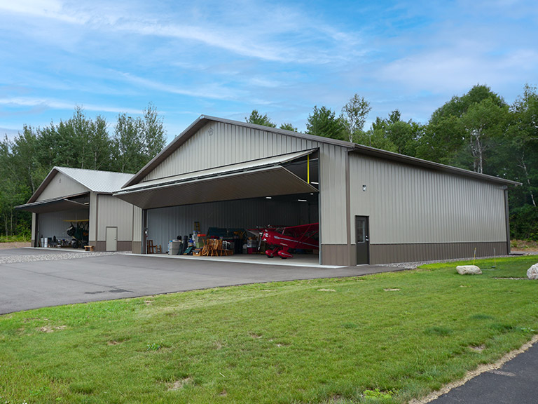 Post-frame airplane hangar with large hydraulic door, steel siding, and aircraft storage space