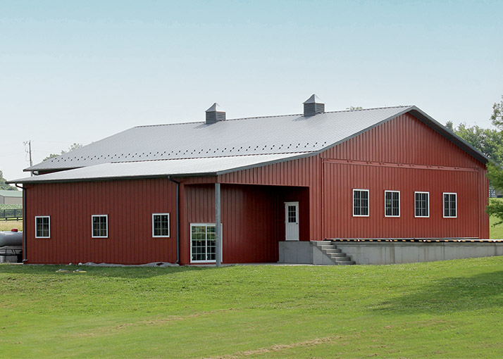 Post-frame airplane hangar with red steel siding, large door opening, and wide-span interior design