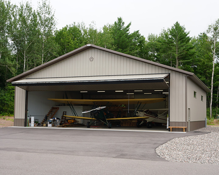 Post-frame airplane hangar with large hydraulic door, steel siding, and multiple aircraft storage