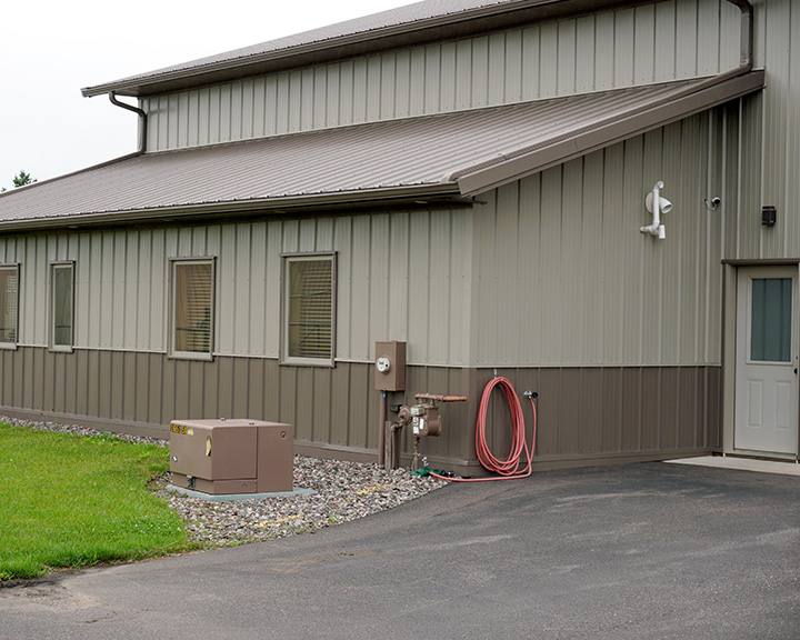 Post-frame airplane hangar exterior with steel siding, service door, and utility connections