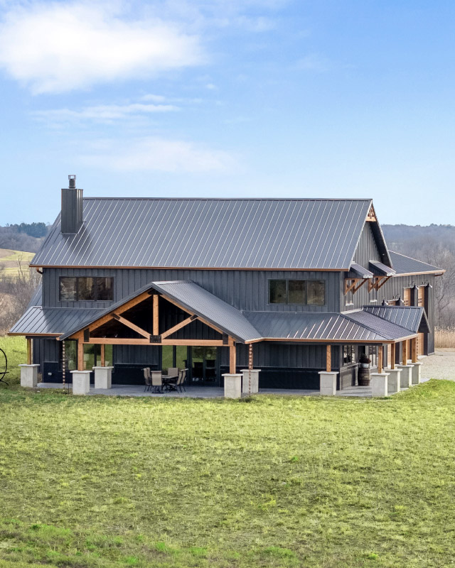 Modern Barndominium with Covered Timber Porch Modern barndominium with black steel siding, metal roof, and covered timber porch
