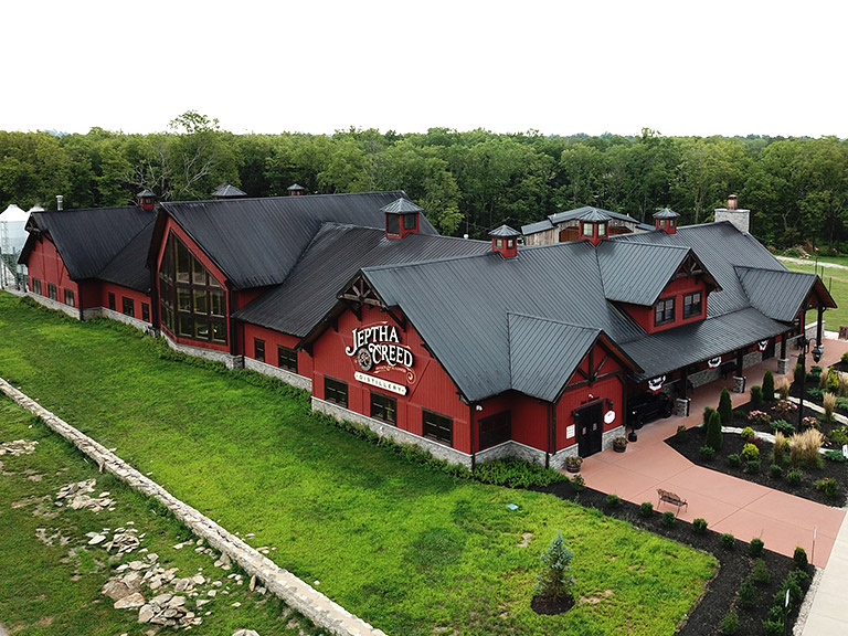 Commercial distillery building with steel siding, multiple rooflines, cupolas, and customer entrance