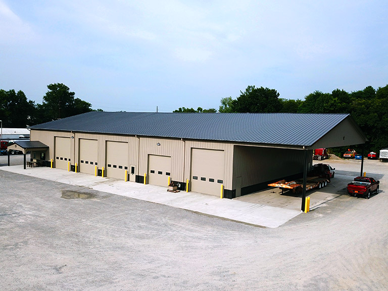 Commercial shop building with steel siding, multiple overhead doors, and covered lean-to for equipment storage