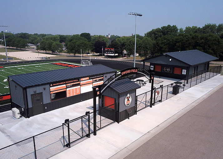 Post frame athletic facility buildings at sports complex with steel siding, scoreboard wall, and stadium field entrance