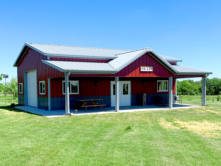 Post-frame garage and shed building with steel siding, overhead door, and covered porch