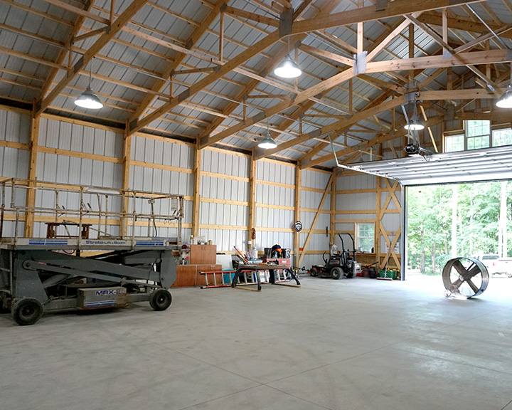 Post-frame garage interior with open floor plan, wood trusses, and overhead door for equipment access