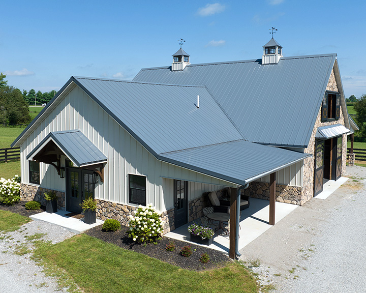 Custom horse barn with stone accents, covered porch, and ventilation cupolas designed for equestrian comfort and style