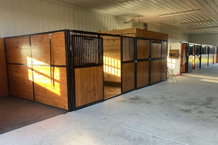 Interior of stall barn showing wooden horse stalls with metal fronts and wide aisle