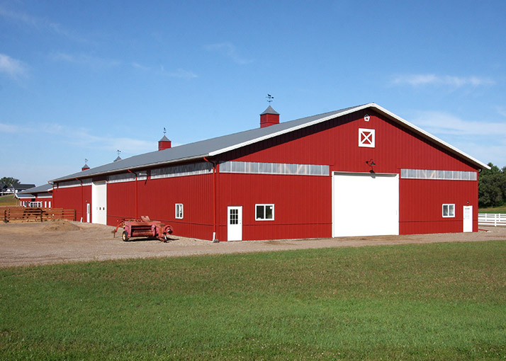 Indoor horse riding arena with steel siding, overhead door, cupolas, and natural light panels