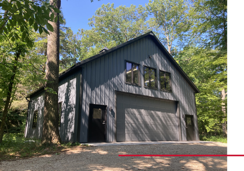 Shop with Living Quarters with Steel Siding and Windows | Walters Buildings Shop with living quarters featuring steel siding, overhead garage door, and multiple windows in wooded setting