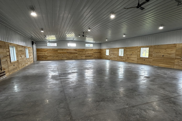 Interior of post frame shop with concrete floor, steel liner ceiling, wood walls, ceiling fans, and multiple windows
