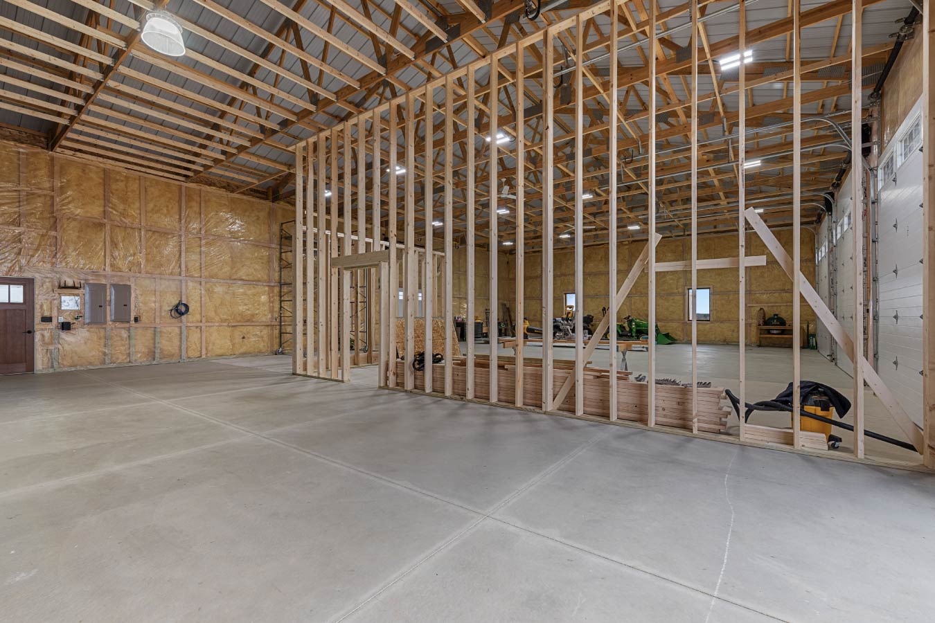 Barndominium workshop interior with open post-frame structure and framed room inside shop