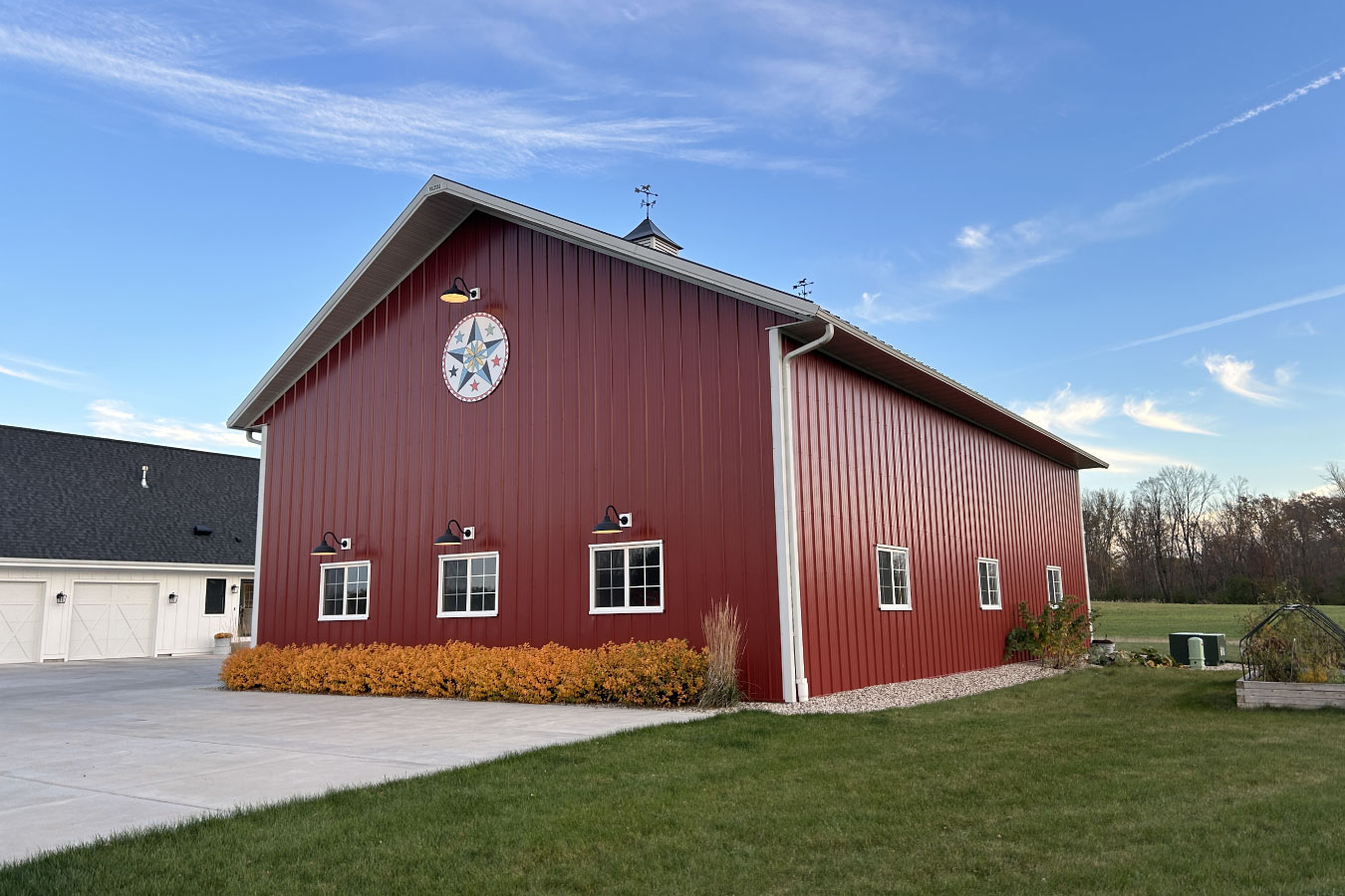 This custom equipment storage building features red steel siding, evenly spaced windows, and a decorative barn star accent centered on the gable. Exterior lighting enhances visibility while the clean layout and durable materials provide long-lasting performance for equipment storage and workshop use.