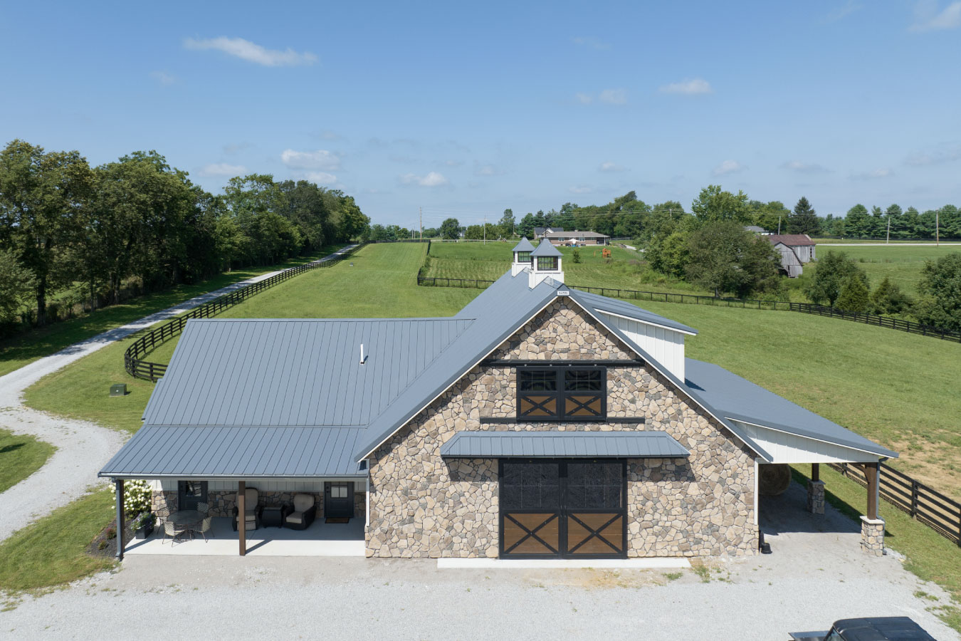 Horse barn with stone exterior, metal roof, and cupola overlooking fenced pasture