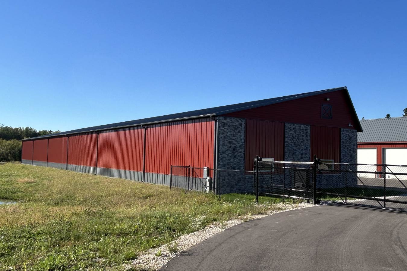 Lone Silo Storage facility in Waukesha Wisconsin with red post frame storage building, gray metal roof, stone accents, and gated entry. Back of Solar Front Storage Building