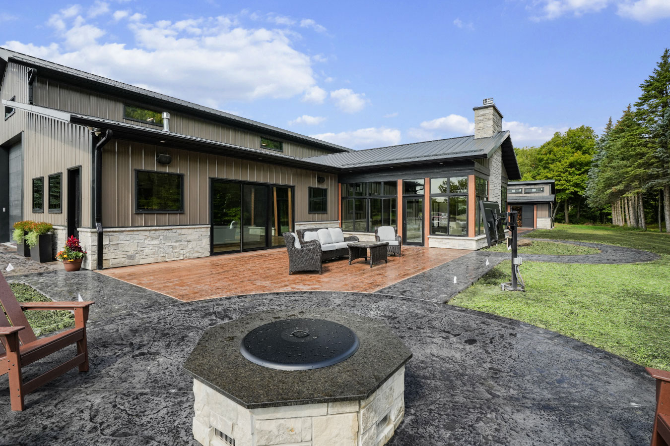 Back patio of a custom monitor barndominium with stamped concrete patio, outdoor fire pit, and large glass windows