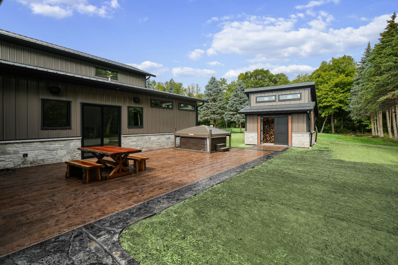 Rear patio of a custom monitor barndominium with stamped concrete patio, outdoor hot tub, and matching storage shed