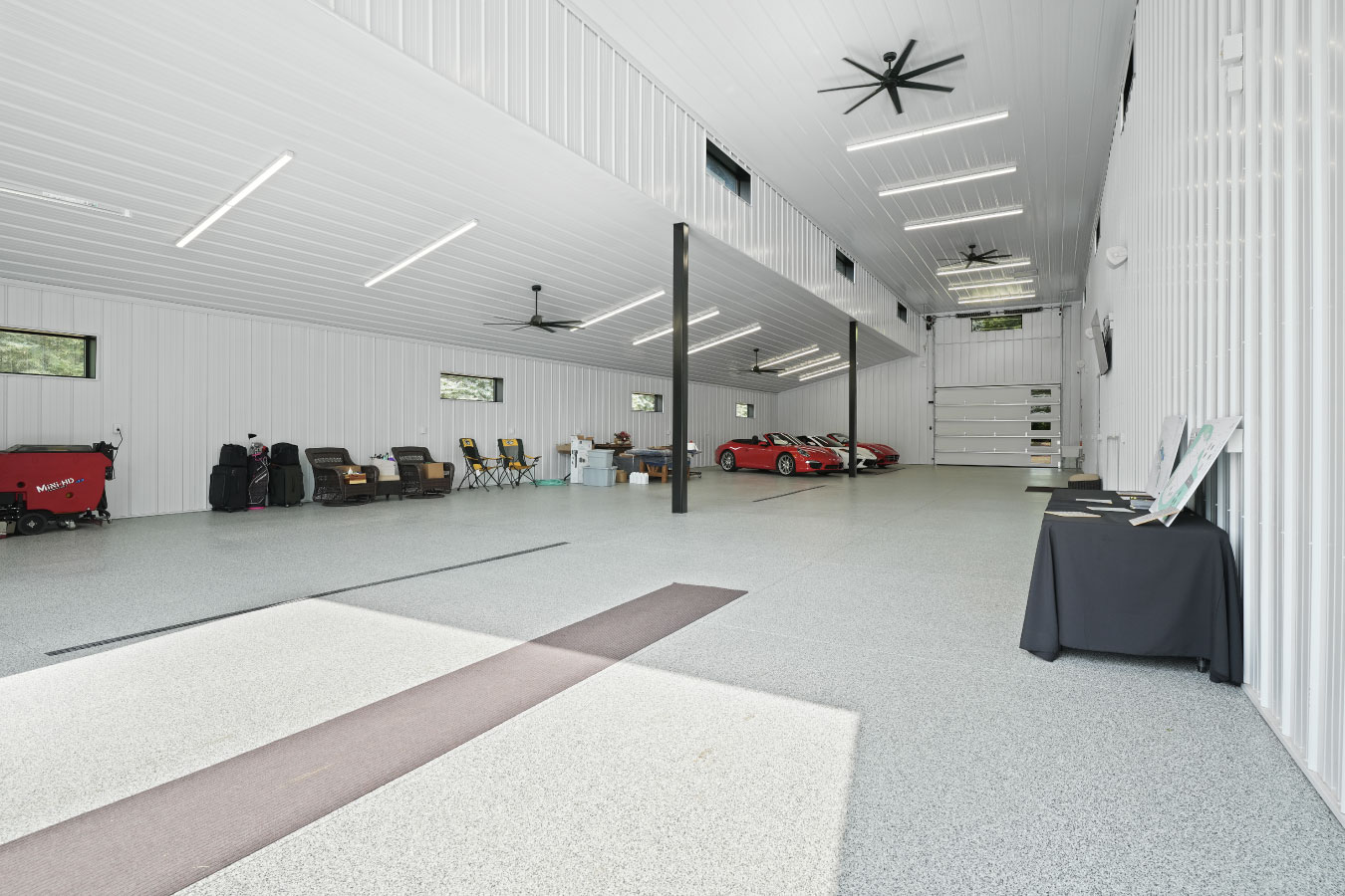 Interior garage of a custom monitor barndominium with high ceilings, white steel liner panels, and space for multiple vehicles