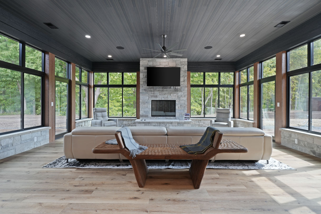 Four-season room in a luxury monitor barndominium with stone fireplace and floor-to-ceiling windows