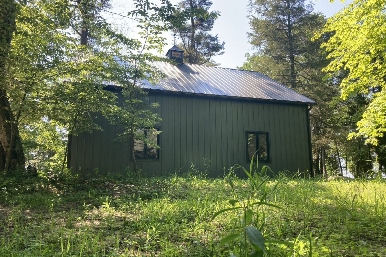 Shop with living quarters with steel siding, windows, and cupola in wooded setting