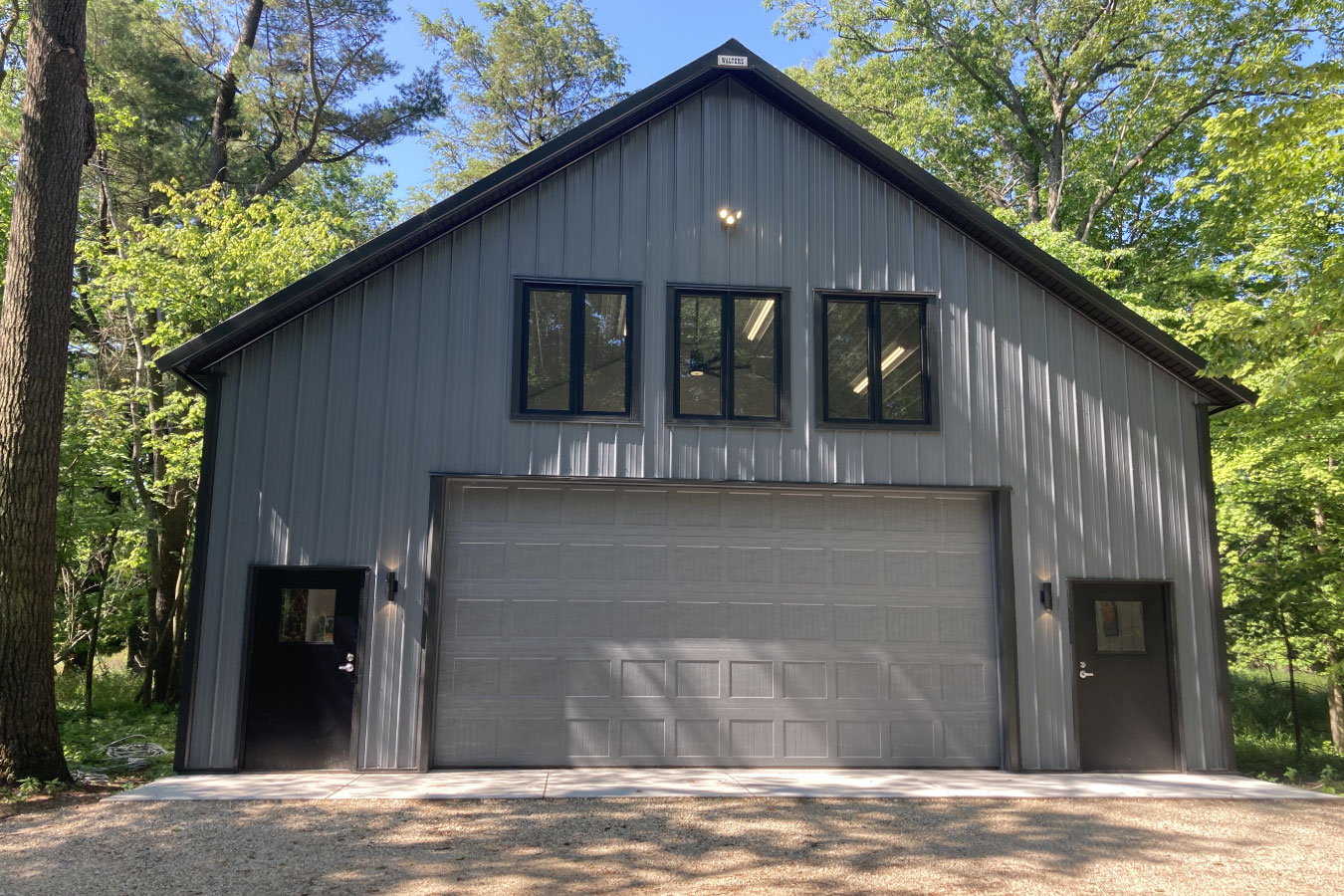 Shop with living quarters with steel siding, overhead garage door, and upper-level windows