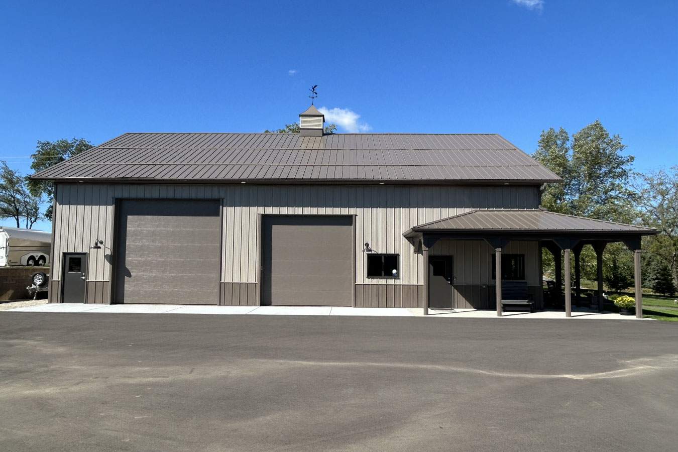 This aerial view highlights a custom man cave garage situated on a spacious rural property. Featuring steel siding, large overhead doors, and a covered porch, the building is designed for both vehicle storage and entertainment. The surrounding land showcases how the garage integrates seamlessly into a private, lifestyle-focused setting.