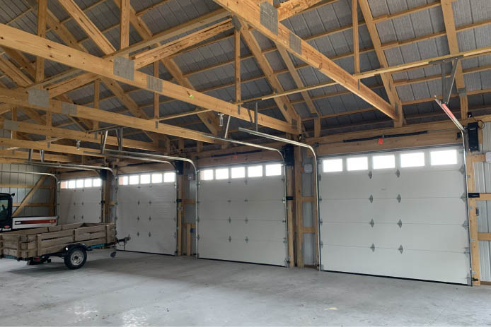 Machinery storage building interior with multiple overhead doors, windows, and open floor space