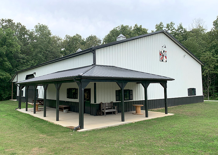 Post-frame hobby workshop with steel siding, covered porch, cupola, and open outdoor workspace area