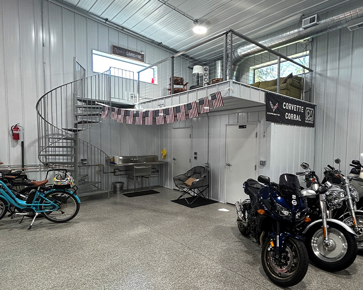 Post-frame hobby workshop interior with loft, spiral staircase, steel liner panels, and motorcycle storage