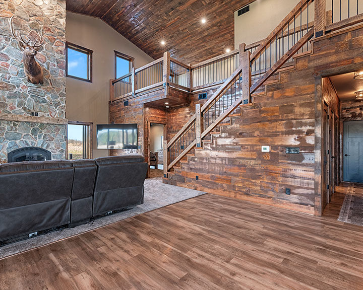 Barndominium interior with open concept layout, loft, wood finishes, staircase, and stone fireplace