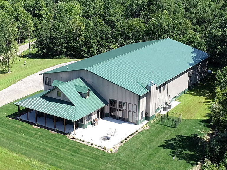 Post-Frame Cabin Hunting Lodge with Covered Porch and Steel Roof Custom post-frame cabin hunting lodge with green steel roof, covered porch, and outdoor patio surrounded by trees