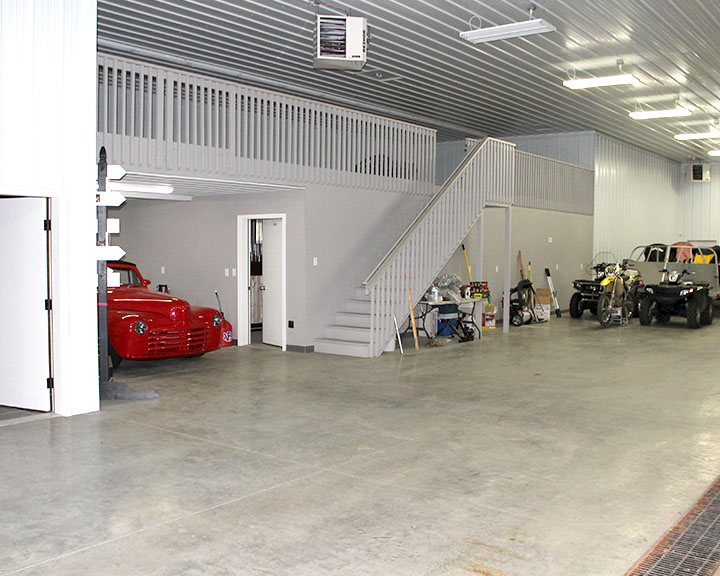 Post-frame cabin garage interior with loft, staircase, concrete floor, and storage space for vehicles and equipment