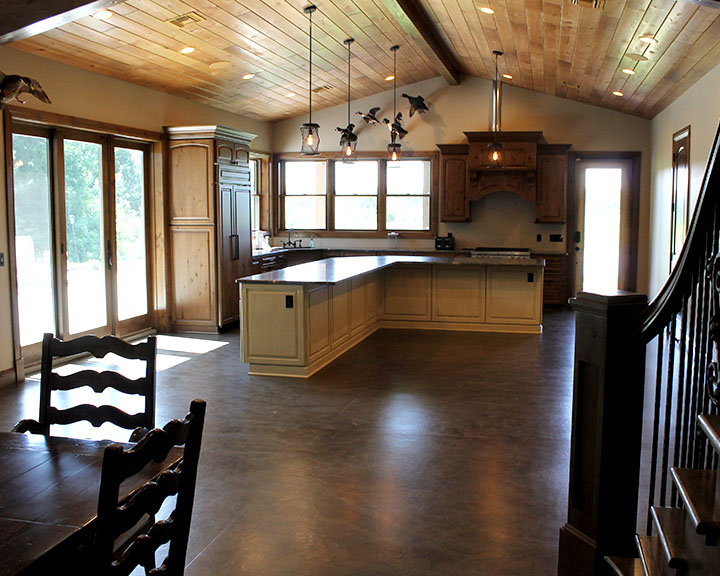 Post-frame cabin kitchen interior with wood ceiling, exposed beams, large windows, and open layout