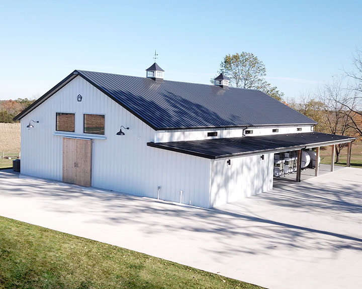 Modern post frame event barn with white steel siding, black steel roof, cupolas, and covered patio for wedding venues