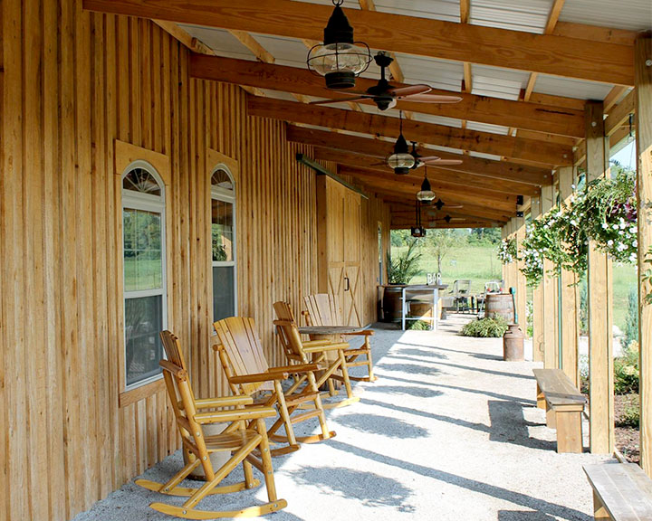 Covered porch on post frame event barn with wood siding, exposed beams, and seating for wedding venue guests