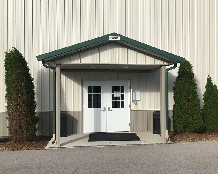 Post frame building entrance with covered porch, steel siding, double walk doors, and protective overhang