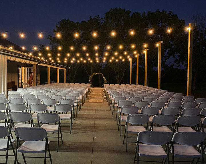 Outdoor wedding ceremony setup at post frame event barn with string lights, seating rows, and ceremony arch