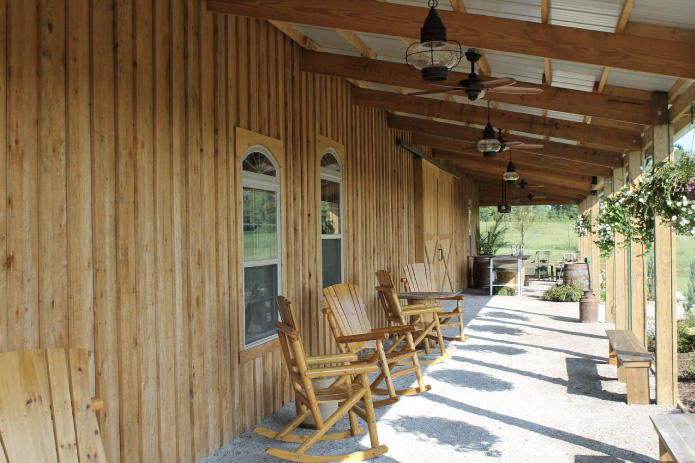Rustic wedding venue covered porch with wooden rocking chairs and exposed timber beams Post-Frame Wedding Barn