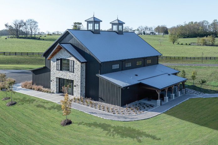 Keene Ranch Event Barn | Custom Post Frame Event Barn by Walters Buildings Keene Ranch event barn with black steel siding, stone exterior, dual cupolas, and covered porch built with post frame construction.