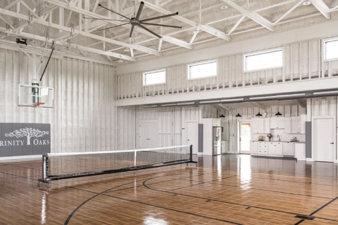 Keene Ranch Event Barn Interior | Post Frame Event Barn Recreation Space indoor Sports Court Interior of the Keene Ranch event barn featuring a recreation court, high post frame ceiling trusses, large ceiling fan, and kitchen area. Indoor Sports Court