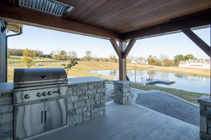 Keene Ranch Event Barn Covered Patio | Outdoor Event Barn Space Covered patio at the Keene Ranch event barn with outdoor kitchen, stone counter, and views of a pond and countryside.
