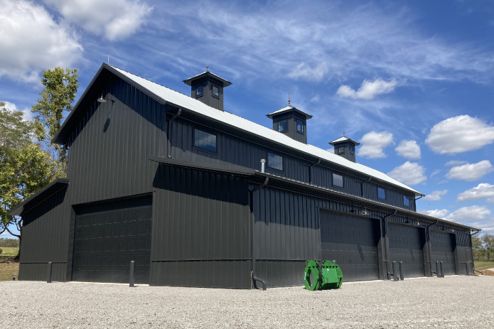 Black monitor barn agricultural storage building with cupolas, clerestory windows, and large overhead equipment doors