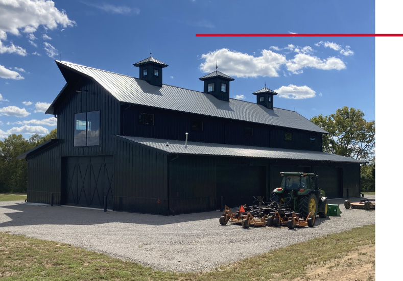 Black monitor barn agricultural storage building with overhead doors and farm equipment parked outside