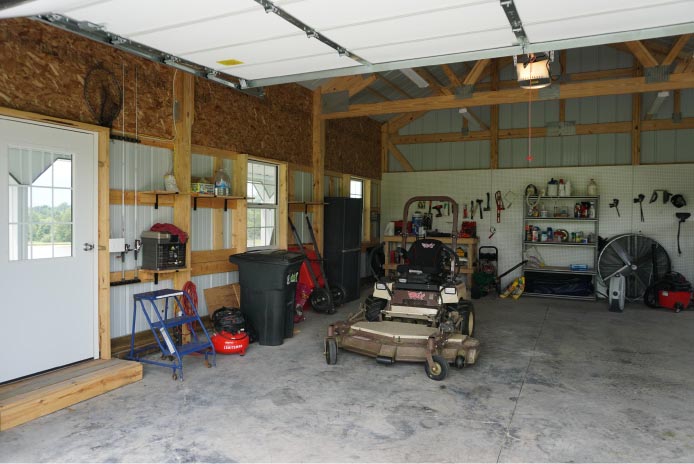Pole Shed Interior with Workshop Setup and Storage | Post Frame Building | Walters Buildings pole shed interior with lawn mower, tools, shelving, and open post frame construction workspace