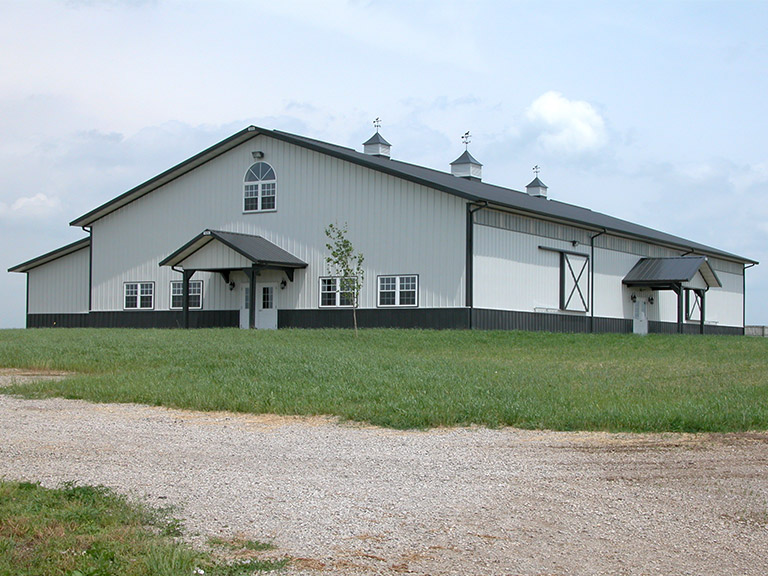 Indoor horse riding arena with steel siding, gable roof, cupolas, and covered entry porch