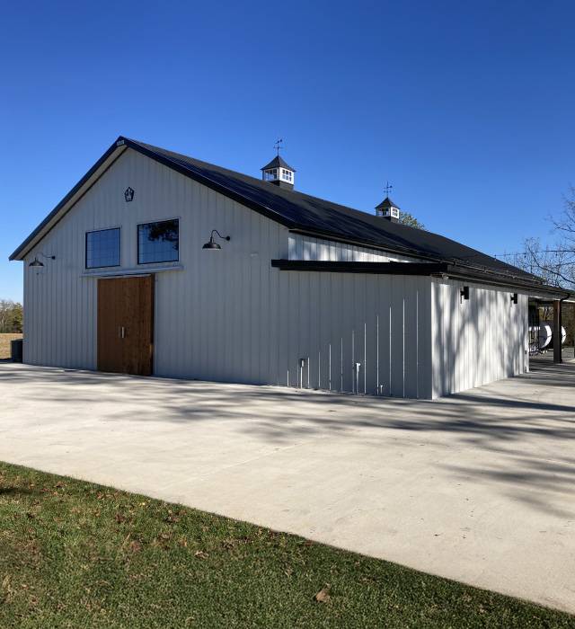 Silo Farms event barn with white steel siding, black metal roof, wooden barn doors, and rooftop cupolas