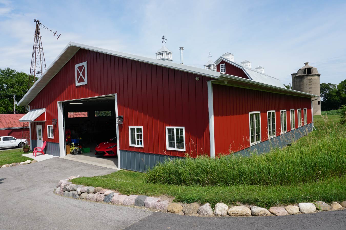 94-0596 car collection garage with red steel siding, large overhead door, side windows, and cupolas